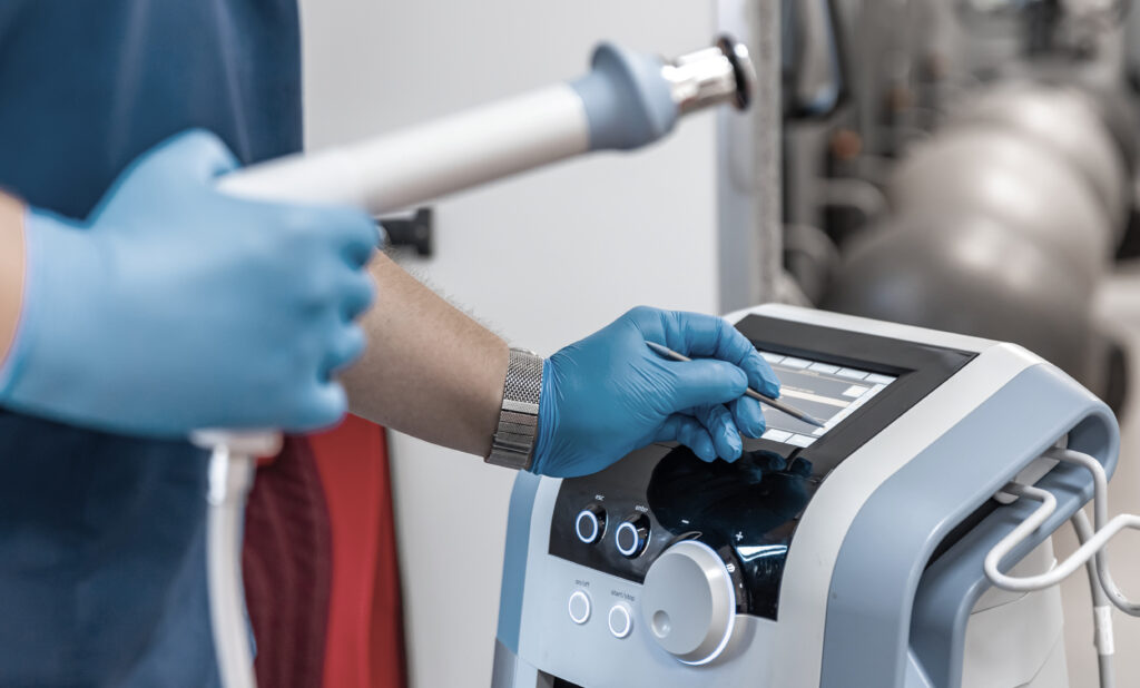 Shock wave therapy device with male doctor hands in rubber gloves.
